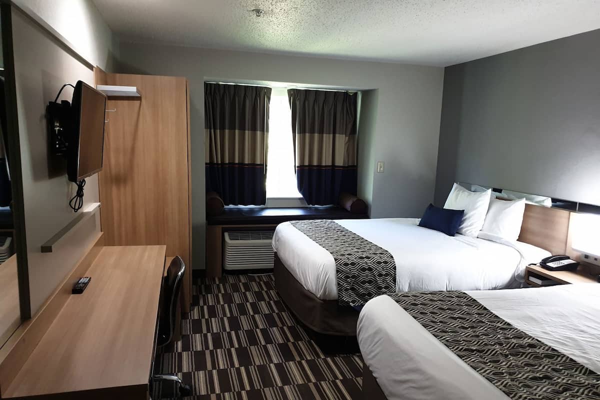 A hotel room with two beds, a desk, a TV, and a window with curtains.
