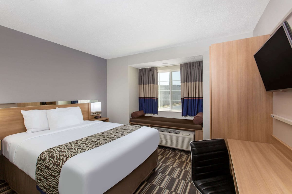 A hotel room with a large bed, a desk, a chair, a TV, and a window with curtains.