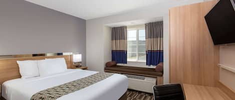 A hotel room with a large bed, a desk, a chair, a TV, and a window with curtains.