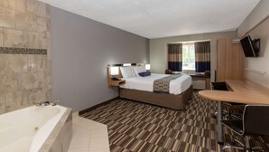 A hotel room with a large bed, a desk, a chair, a flat-screen TV, and a bathroom with a bathtub. - Microtel Inn & Suites by Wyndham Augusta/Riverwatch (Augusta)
