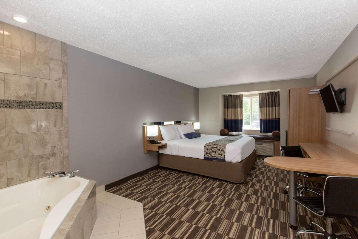 A hotel room with a large bed, a desk, a chair, a flat-screen TV, and a bathroom with a bathtub.