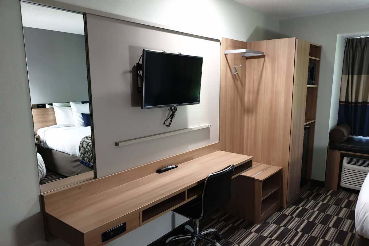 A hotel room with a wooden desk, a mounted TV, a mirror, and a wardrobe.