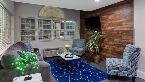 A modern living room with a sofa, two patterned armchairs, a coffee table, and a large window with blinds. - Microtel Inn & Suites by Wyndham Augusta/Riverwatch (Augusta)
