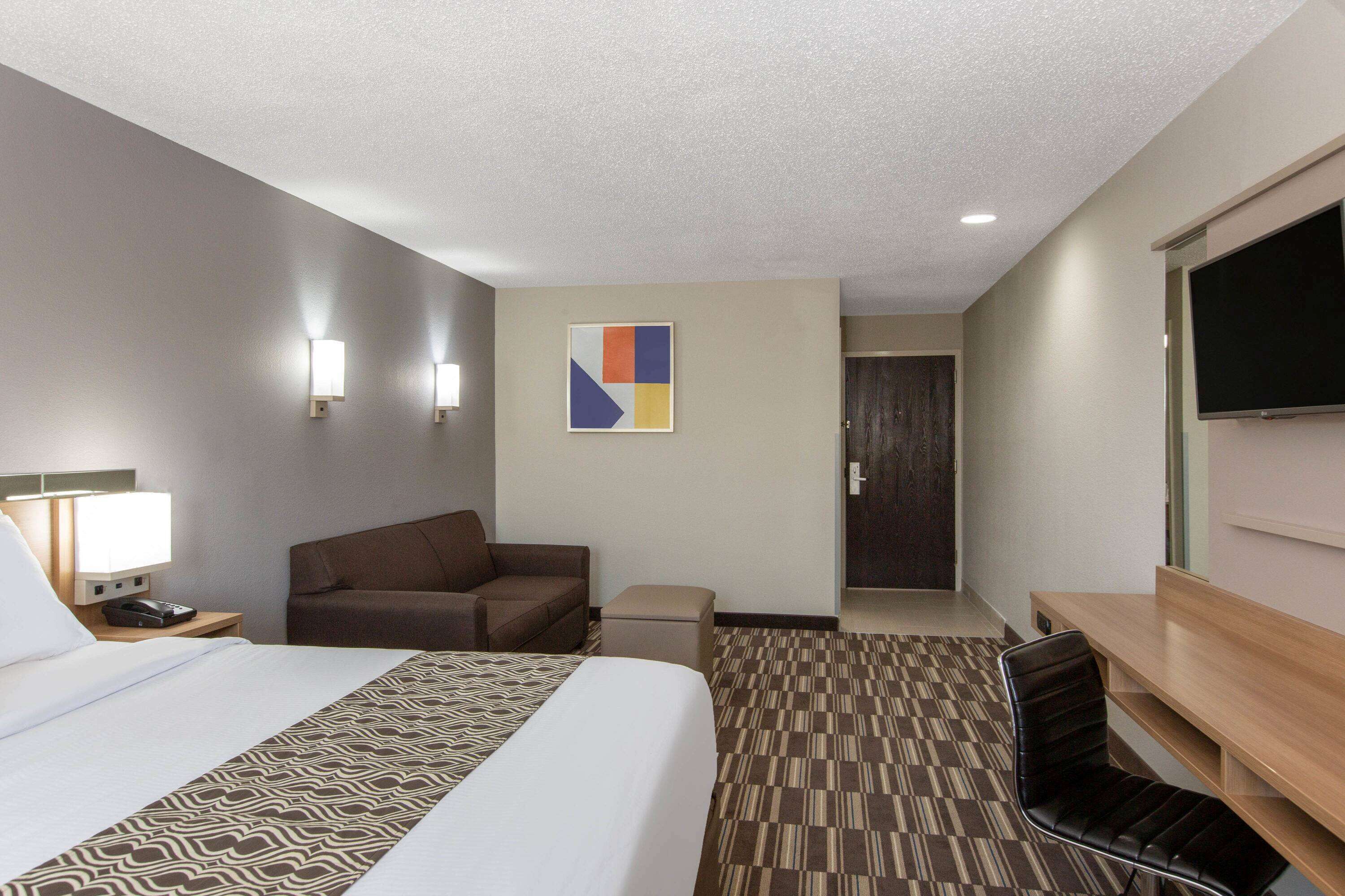 Una habitación de hotel con una cama grande, un escritorio, una silla, un sofá y un televisor.