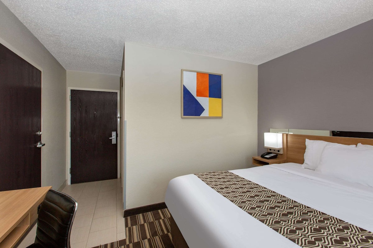 A hotel room with a bed, bedside table, lamp, and a painting on the wall.