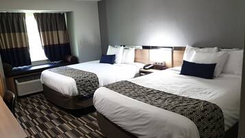 Une chambre d’hôtel avec deux lits, un bureau et une fenêtre avec des rideaux.