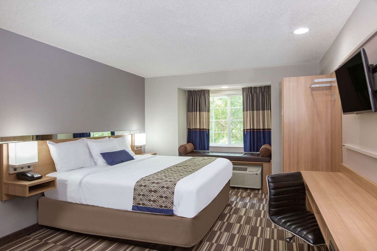 A hotel room with a bed, bedside tables, a desk, a chair, a TV, and a window with curtains.