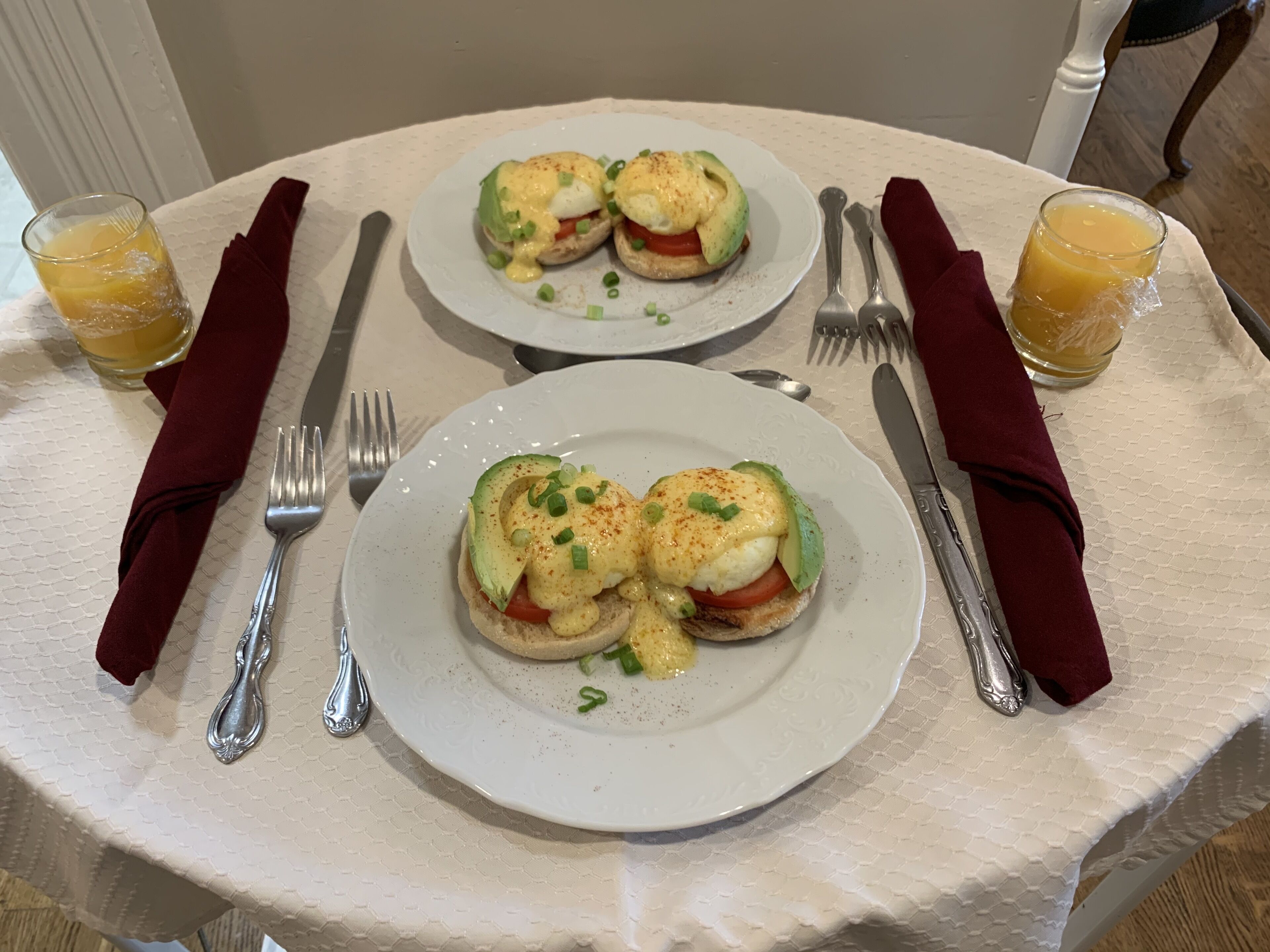 Una tavola apparecchiata con due piatti di uova alla Benedict, due bicchieri di succo d'arancia e posate con tovaglioli rossi.