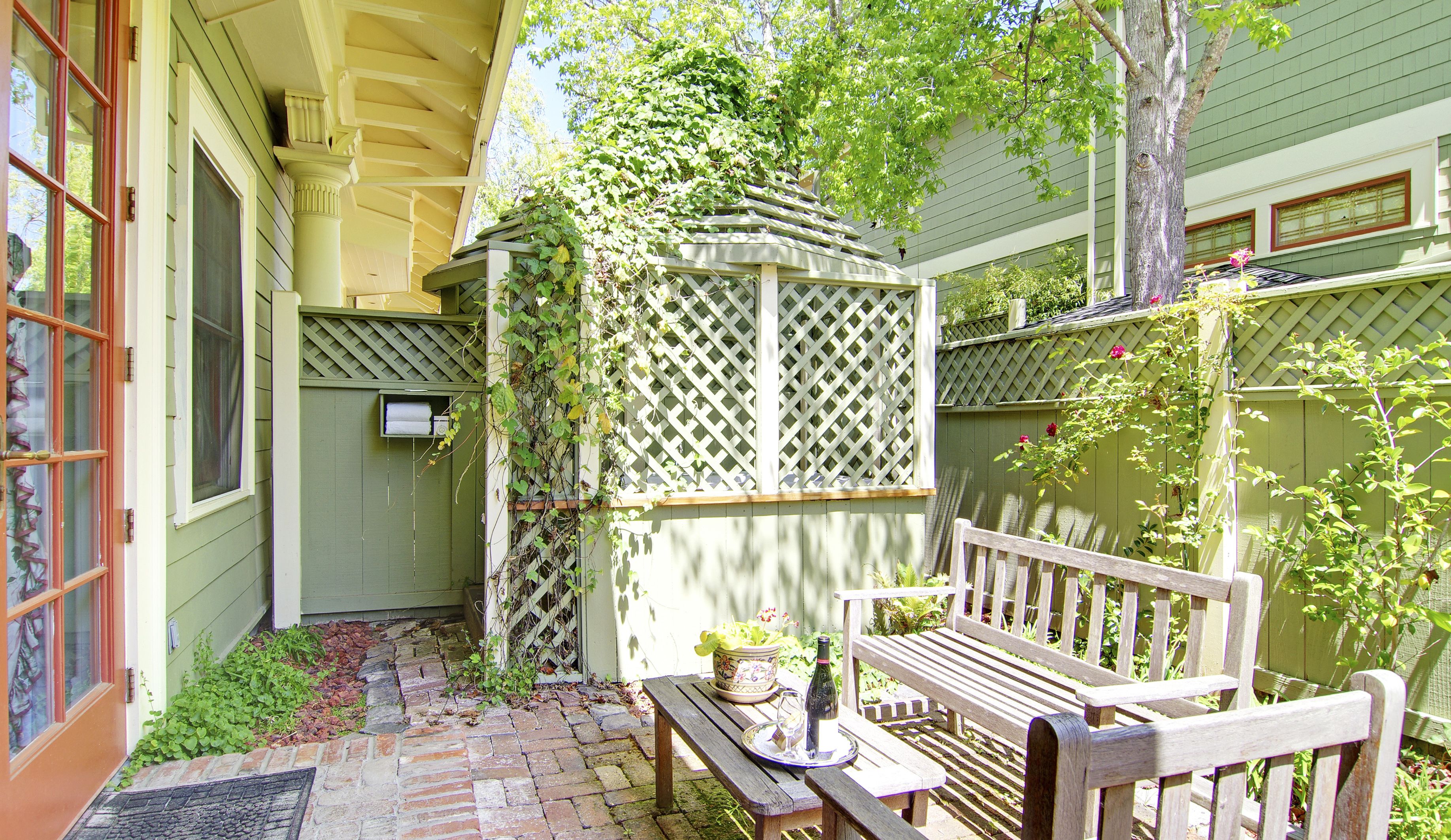 A wooden bench with a tray, a potted plant, and a bottle, set against a green fence with climbing plants.