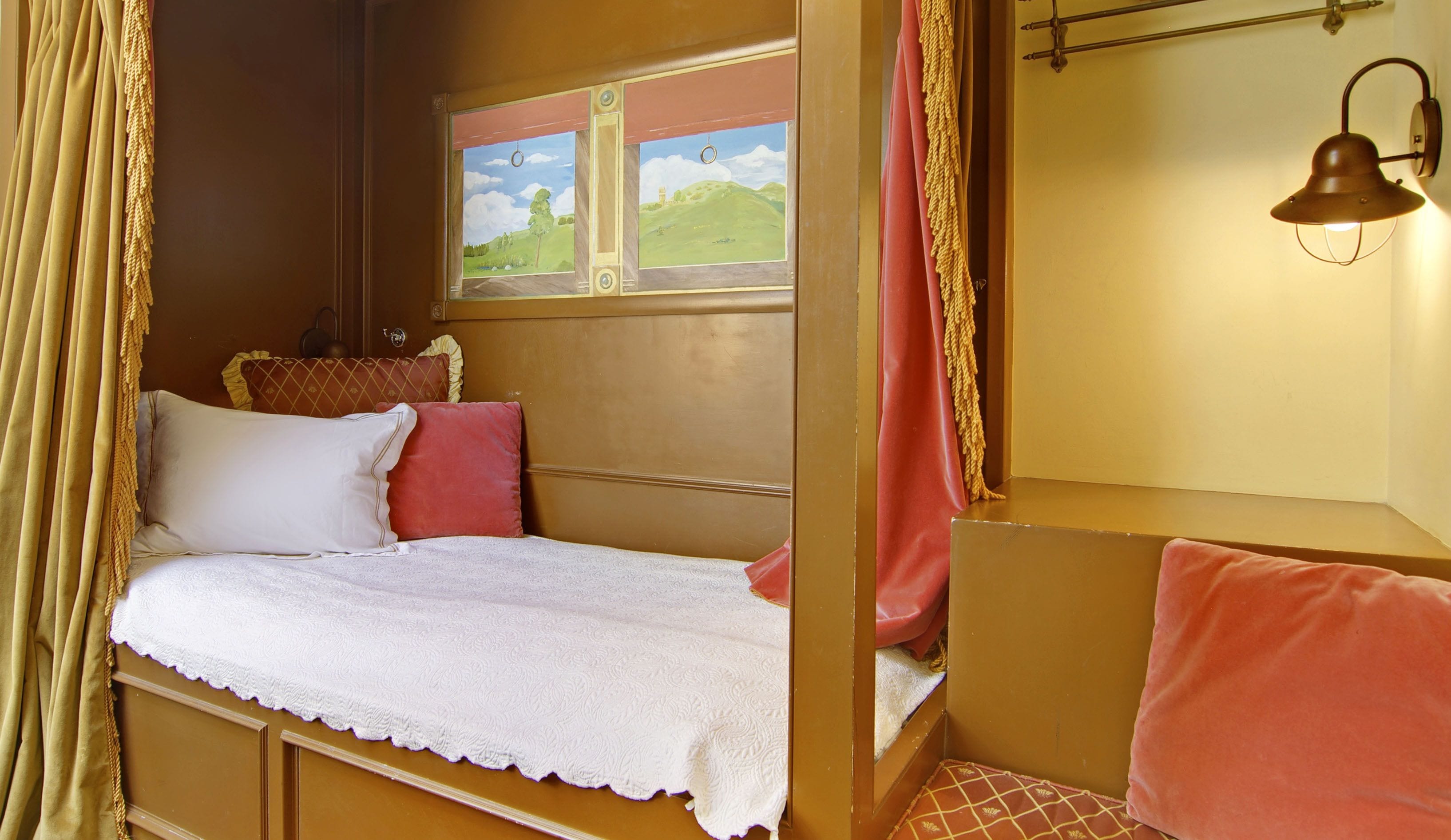 Un dormitorio acogedor con una cama individual, una ventana que da a un paisaje verde y una lámpara fijada a la pared.