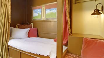 Un dormitorio acogedor con una cama individual, una ventana que da a un paisaje verde y una lámpara fijada a la pared.