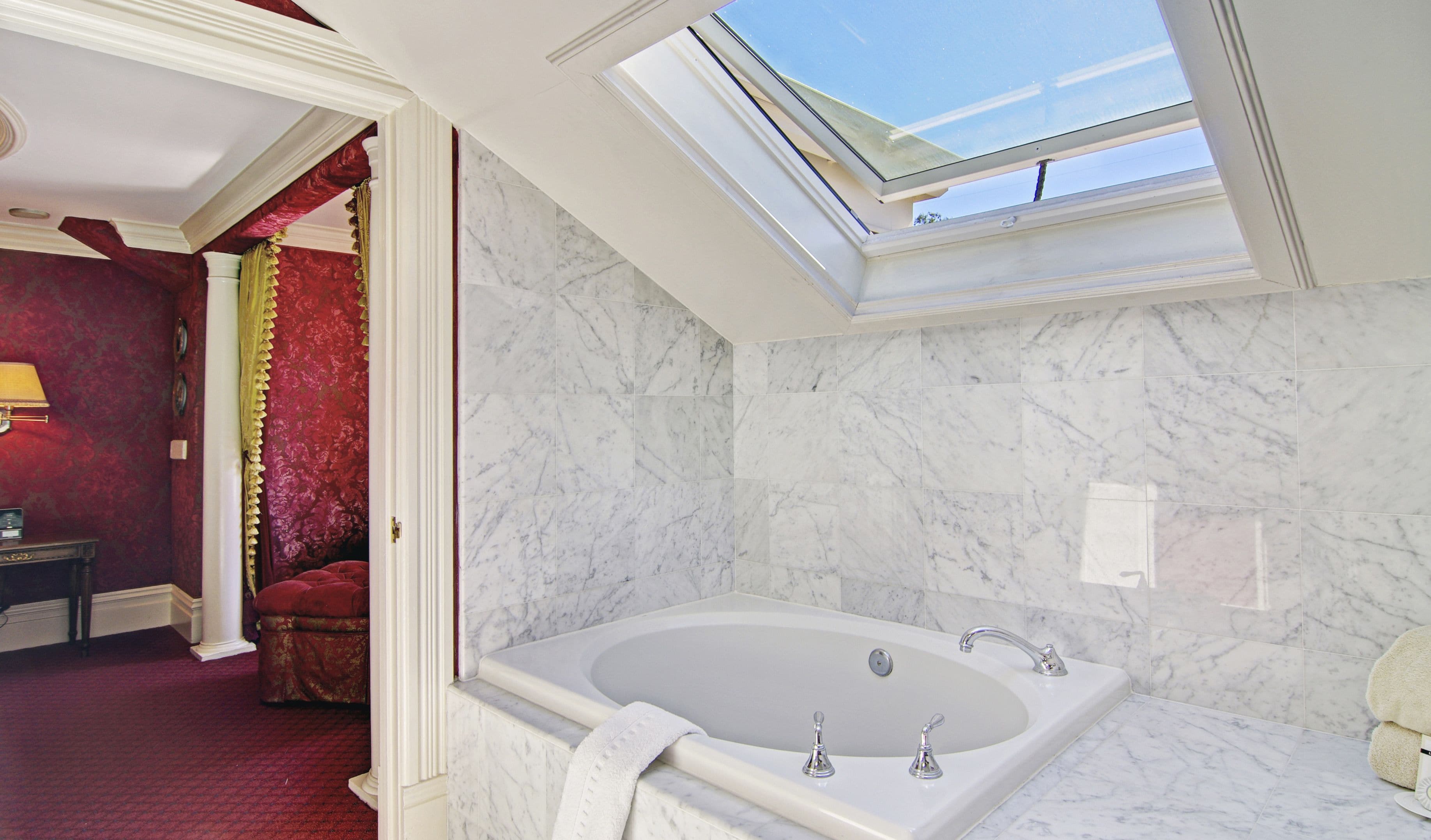 Un baño moderno con tragaluz, paredes de mármol y una bañera grande.