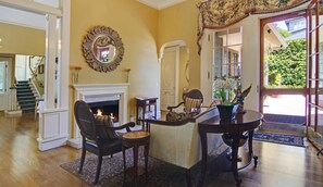 A room with a fireplace, a dining table, and a chair. There is a mirror on the wall and a door leading outside. - Inn at Depot Hill (Capitola)