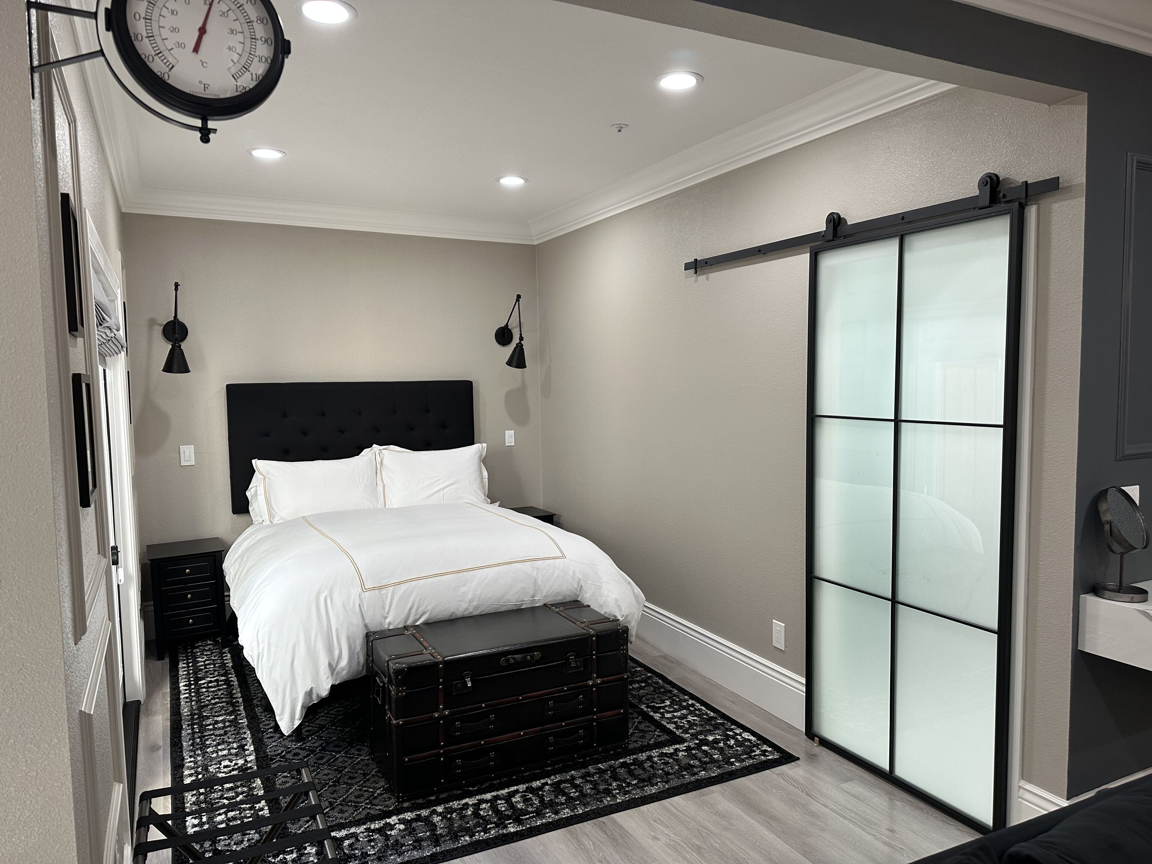 Un dormitorio moderno con una cama grande, un cabecero negro, un reloj de pared y una puerta corrediza de vidrio.