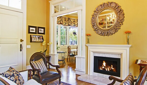 A living room with a fireplace, a large mirror, and a dining area visible through an open door. - Inn at Depot Hill (Capitola)
