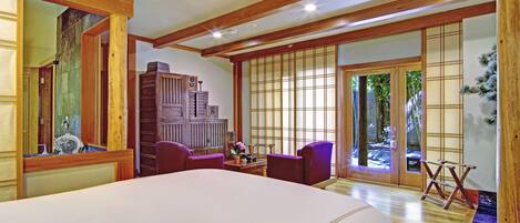 A spacious bedroom with a large bed, wooden beams, a traditional Japanese sliding door, and a small table with chairs.