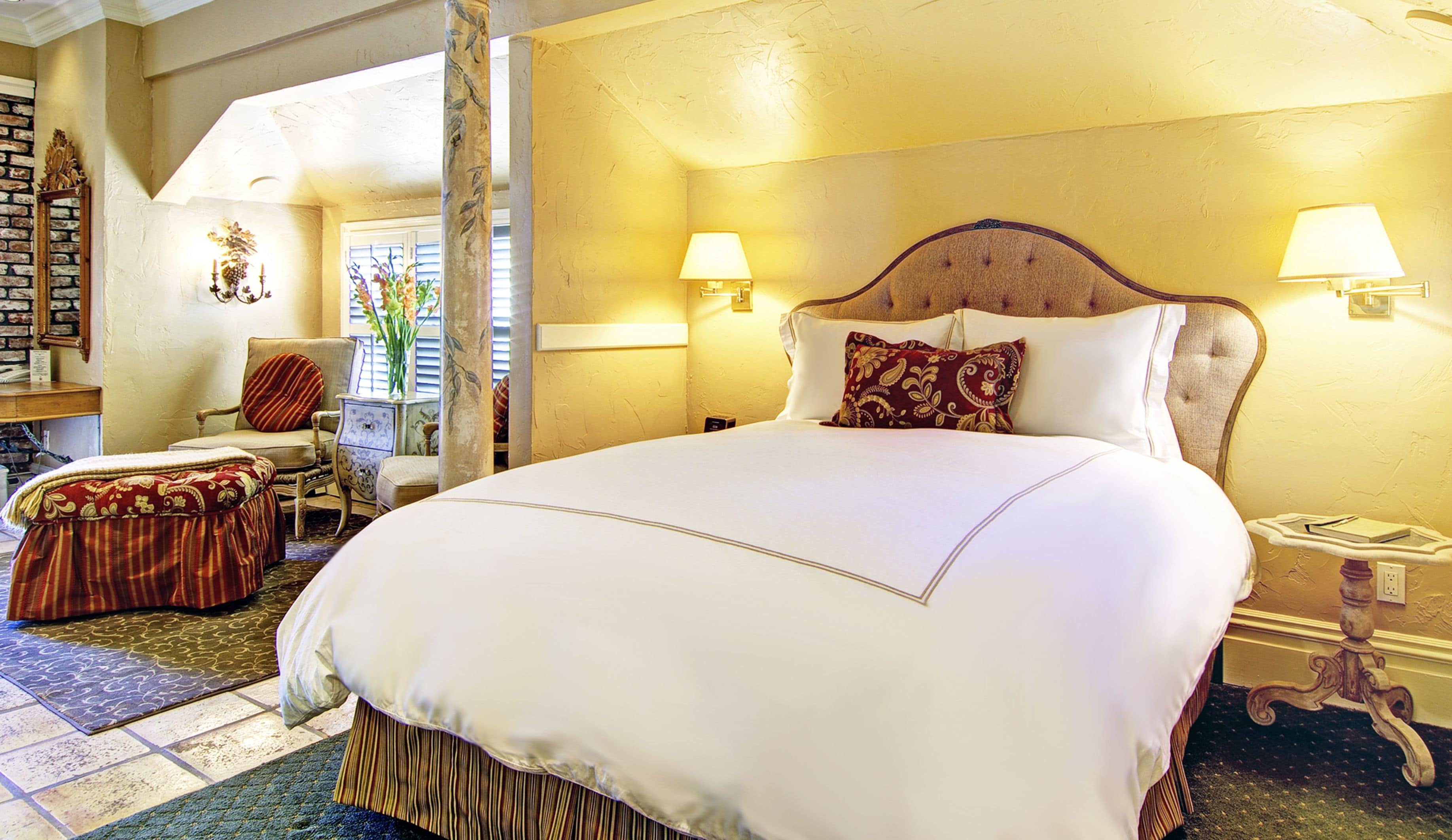 Una cama grande con cabecera de madera, dos lámparas de noche y un arreglo floral sobre una mesita.