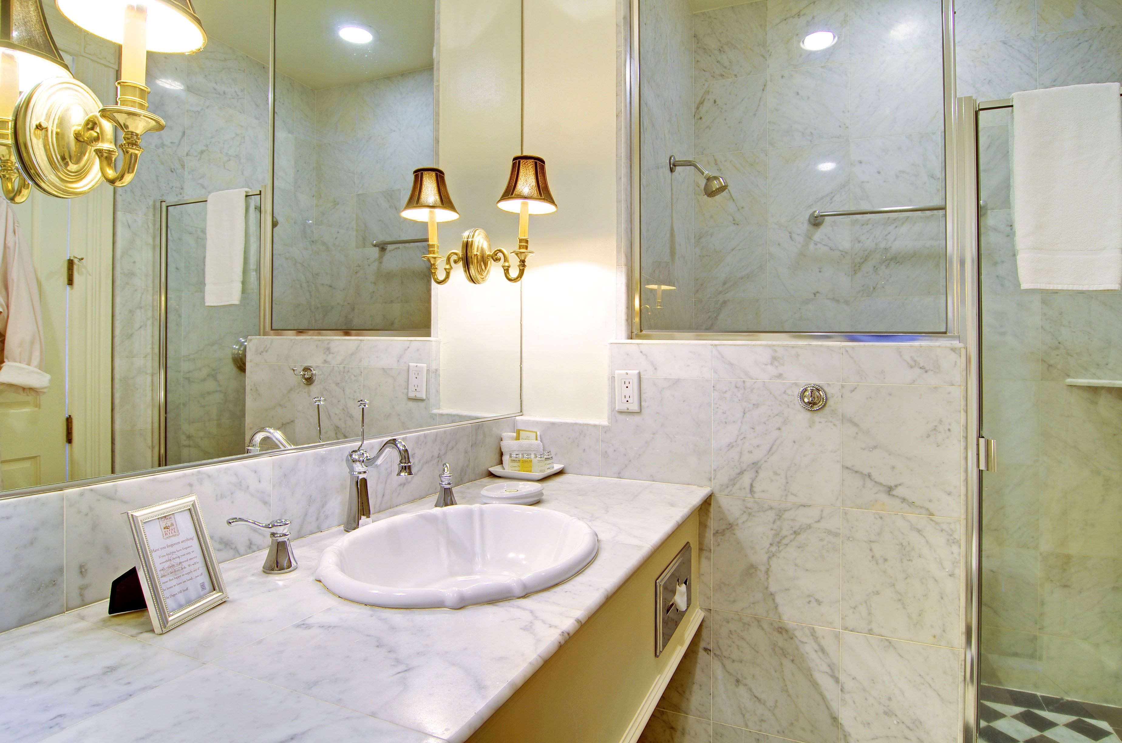 A bathroom with a marble sink, two wall-mounted lamps, a large mirror, and a glass-enclosed shower.