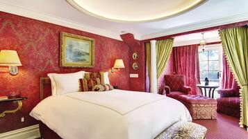 A hotel room with a large bed, a chair, a table, and a painting on the wall.