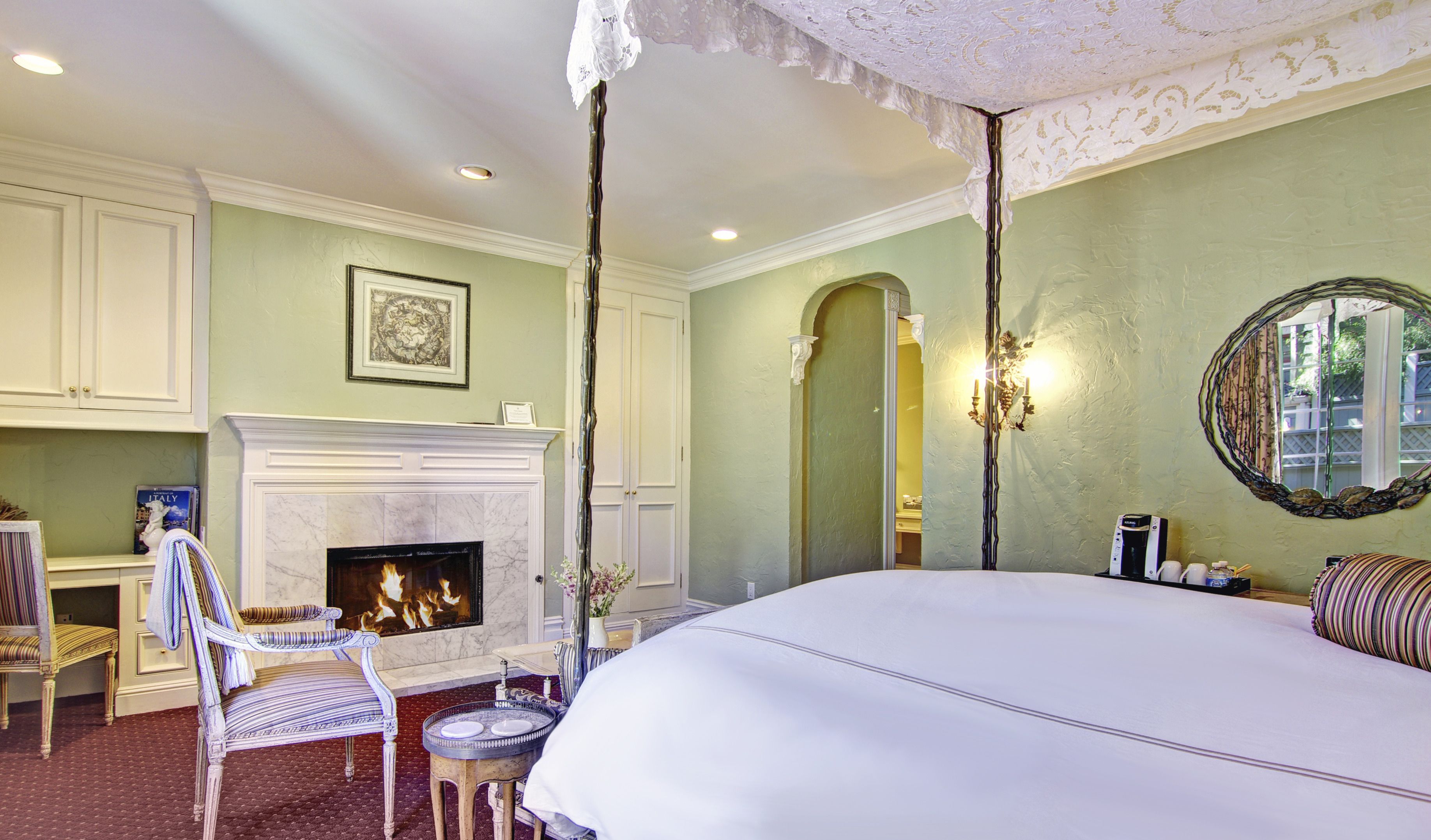 A bedroom with a large bed, a fireplace, a chair, and a table.