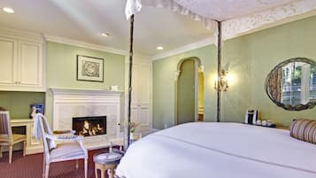 A bedroom with a large bed, a fireplace, a chair, and a table.