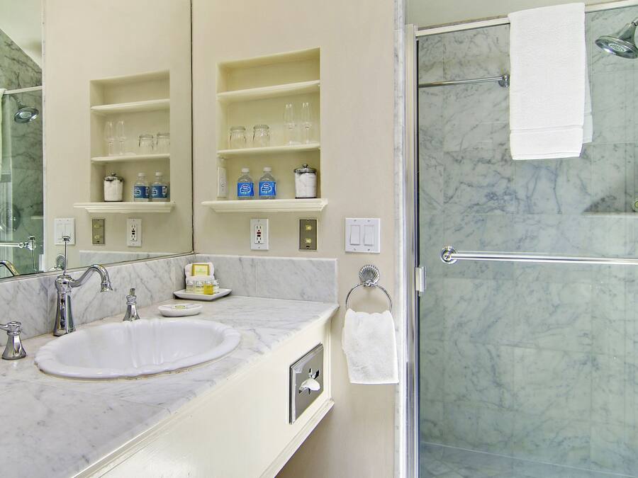 A bathroom with a marble sink, a glass-enclosed shower, and shelves with toiletries.