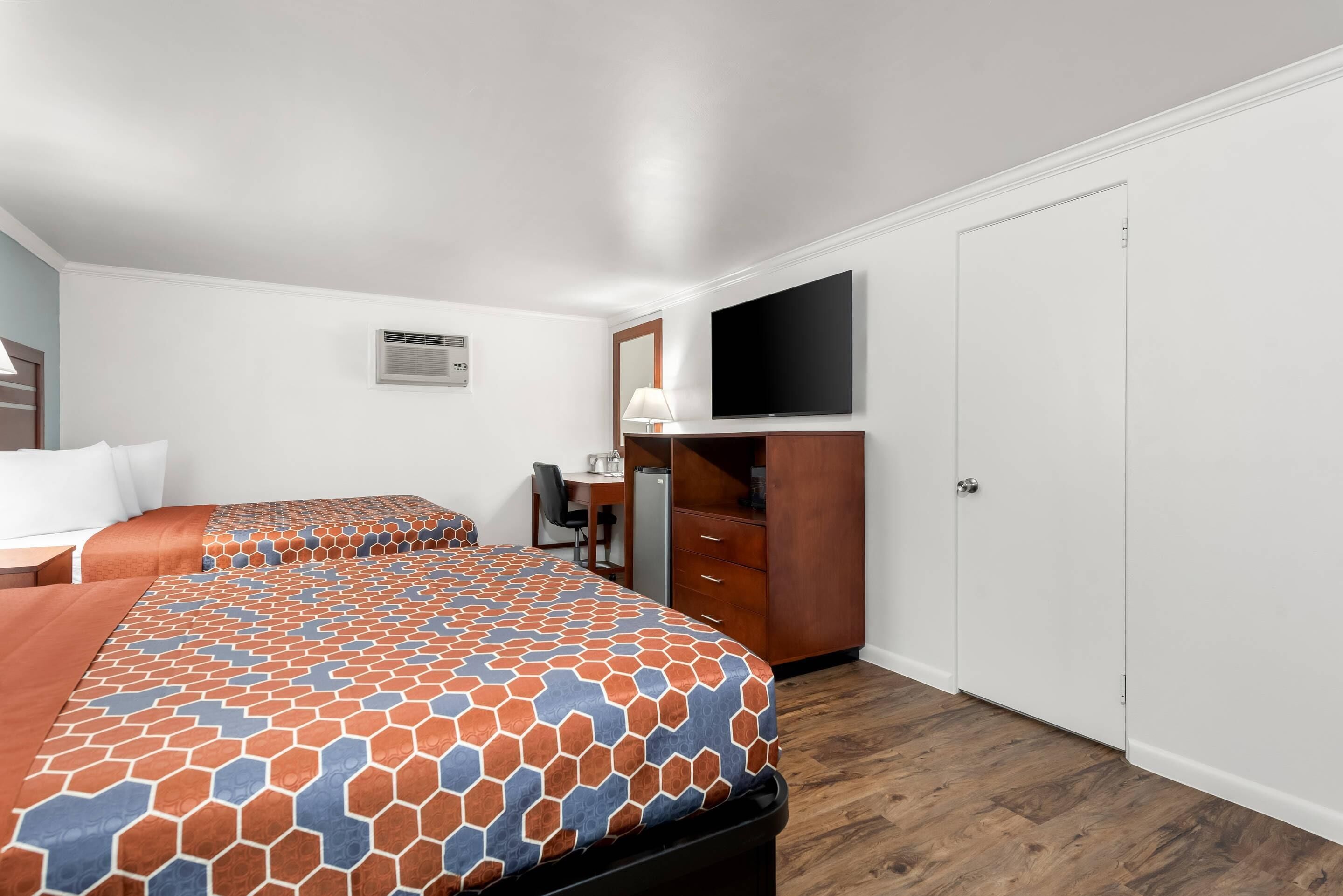 A hotel room with two beds, a desk, a chair, a television, and a wardrobe.