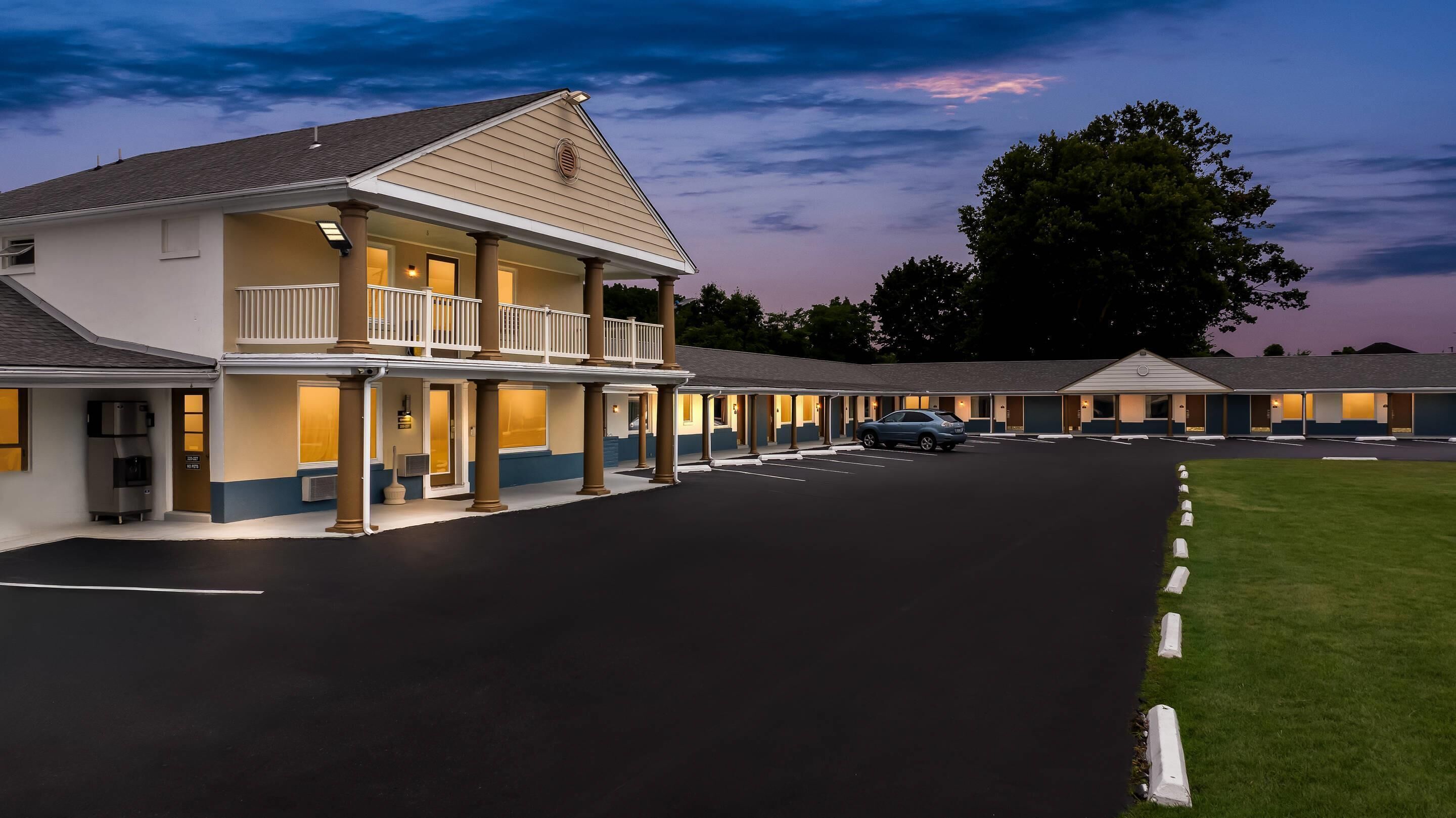 A motel with a two-story structure, a covered parking area, and a well-maintained lawn.