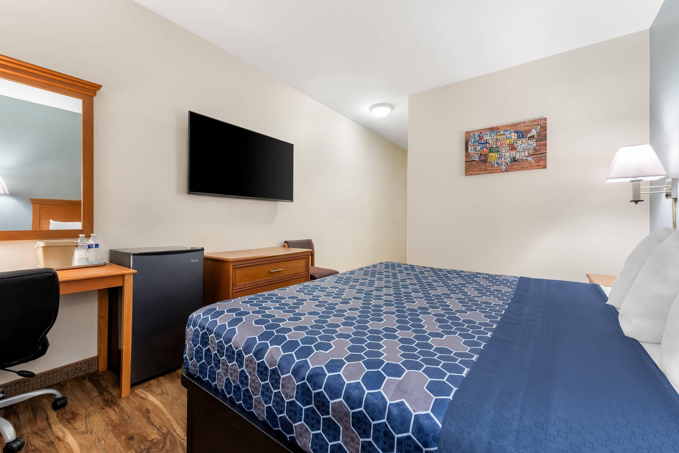 A hotel room with a bed, a desk, a chair, a television, and a wall-mounted artwork.