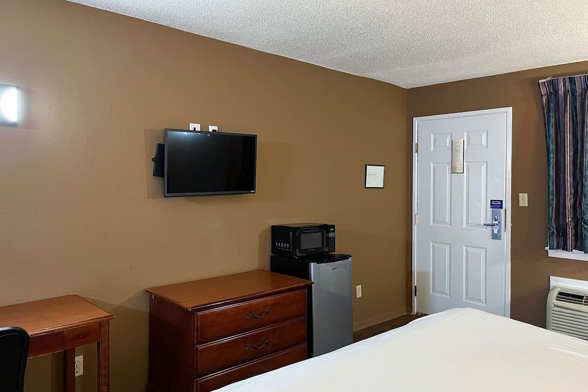 A hotel room with a bed, a dresser, a desk, a television, a microwave, a mini-fridge, and a door with a sign.