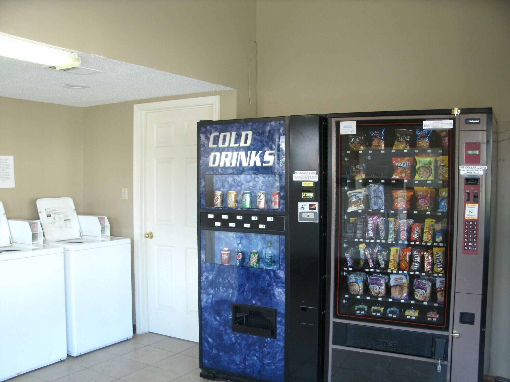 A vending machine with a 'Cold Drinks' sign, a coin-operated snack machine, and a white counter with a paper sign.