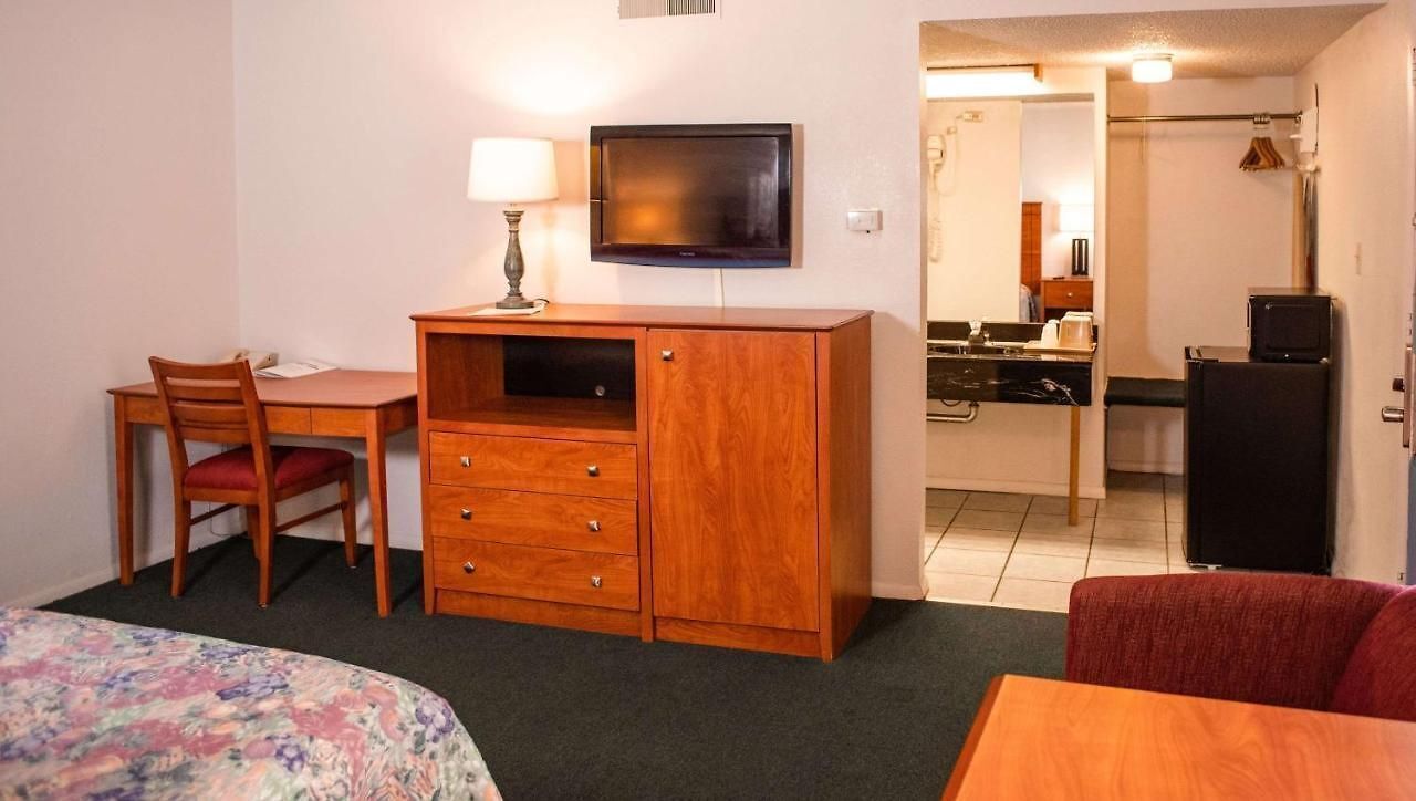 Quarto de hotel com cama, escrivaninha, cadeira, televisão, cozinha compacta e um pequeno frigorífico.