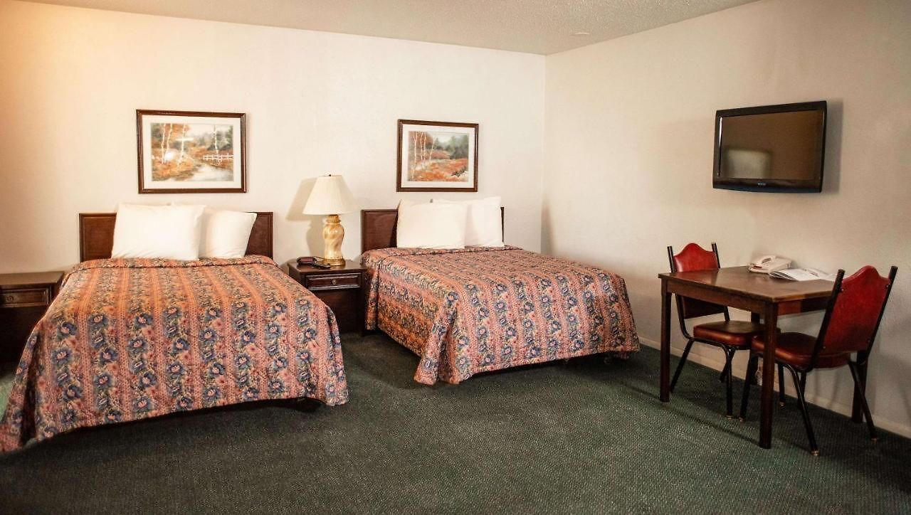 Habitación de hotel con dos camas, un escritorio, una silla, un televisor y dos cuadros en la pared.