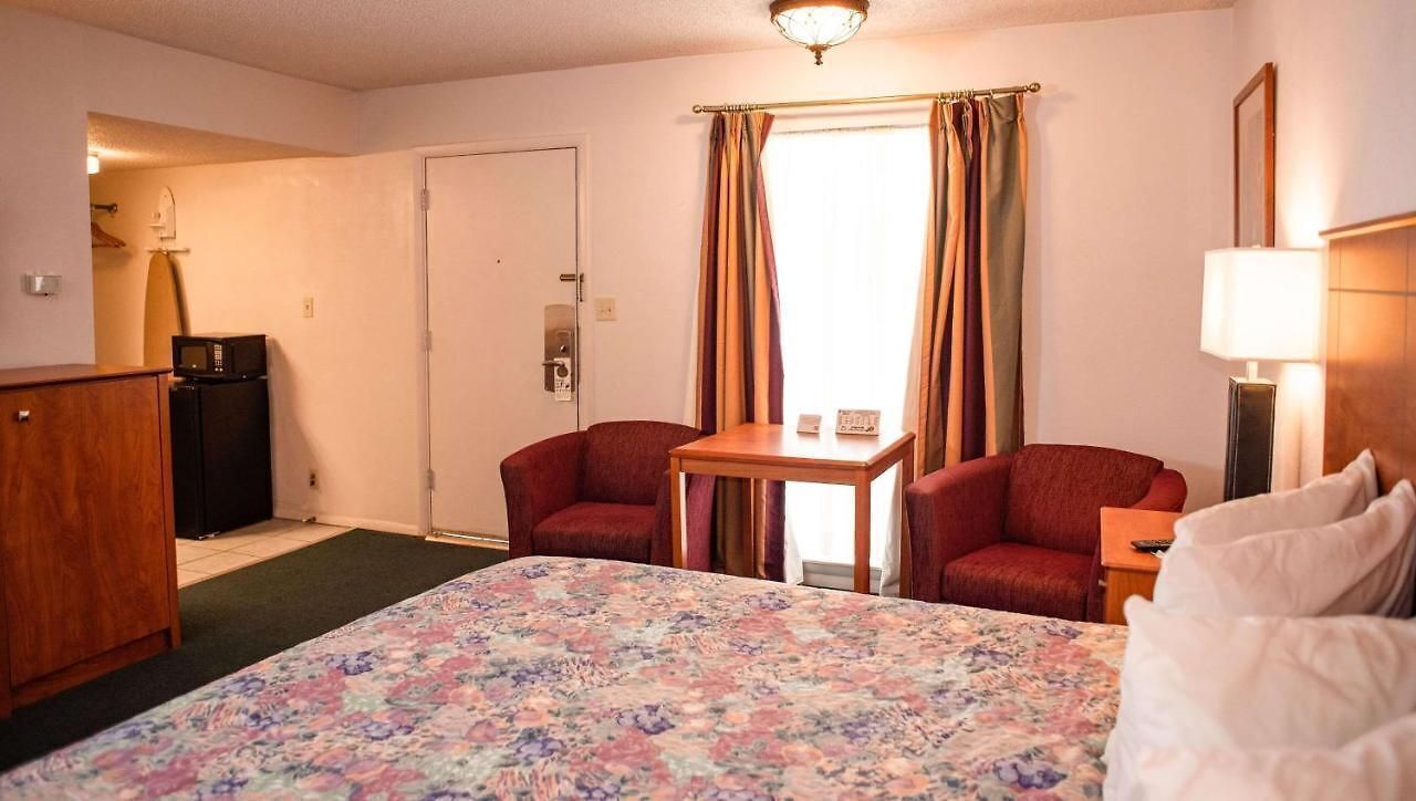 Une chambre d’hôtel avec un lit, deux fauteuils rouges, une petite table, un bureau, un four à micro-ondes, un réfrigérateur et une porte.