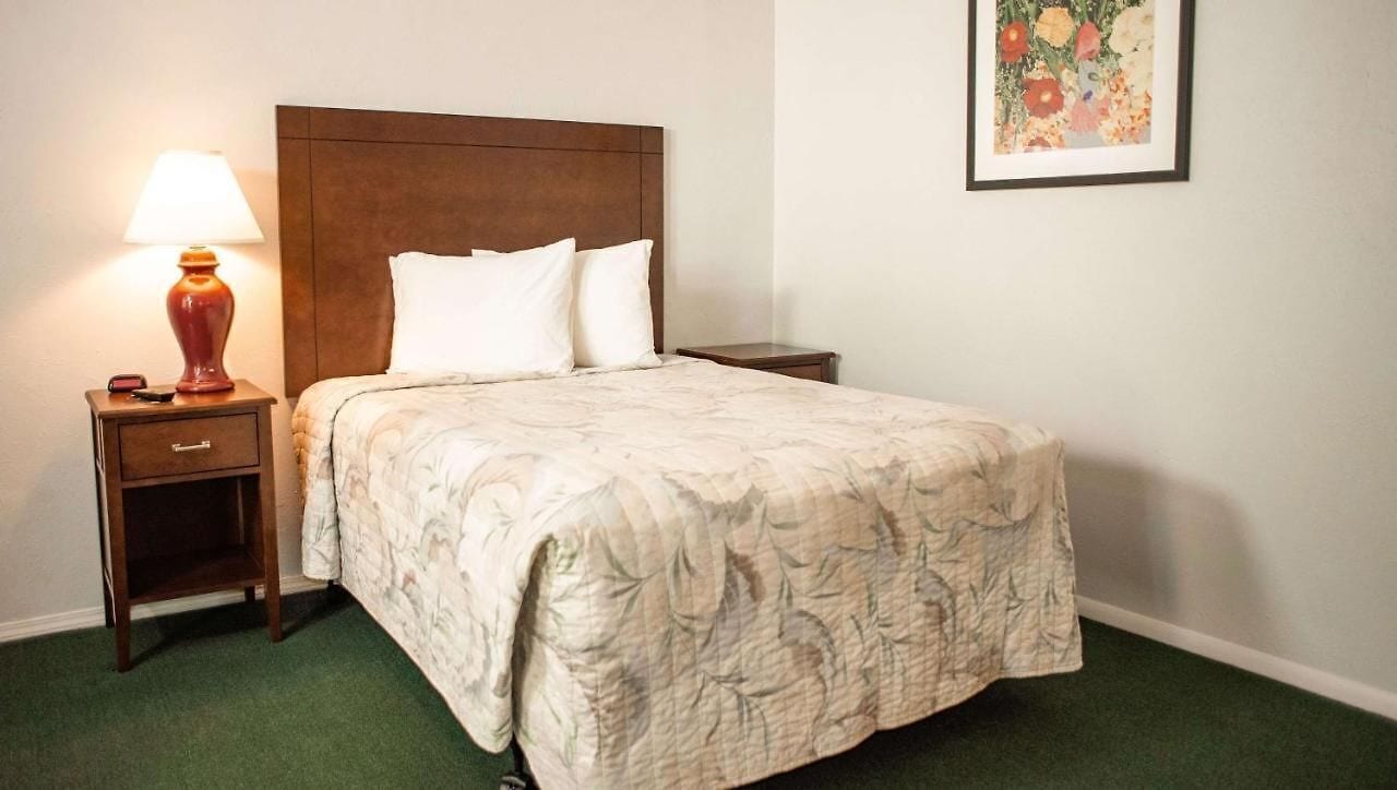 Una cama bien hecha con colcha estampada de flores, una mesita de noche de madera con lámpara y una obra de arte floral enmarcada en la pared.