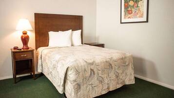 Una cama bien hecha con colcha estampada de flores, una mesita de noche de madera con lámpara y una obra de arte floral enmarcada en la pared.