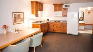 A compact kitchen with wooden cabinets, a white refrigerator, a microwave, and a dining area with a table and chairs.