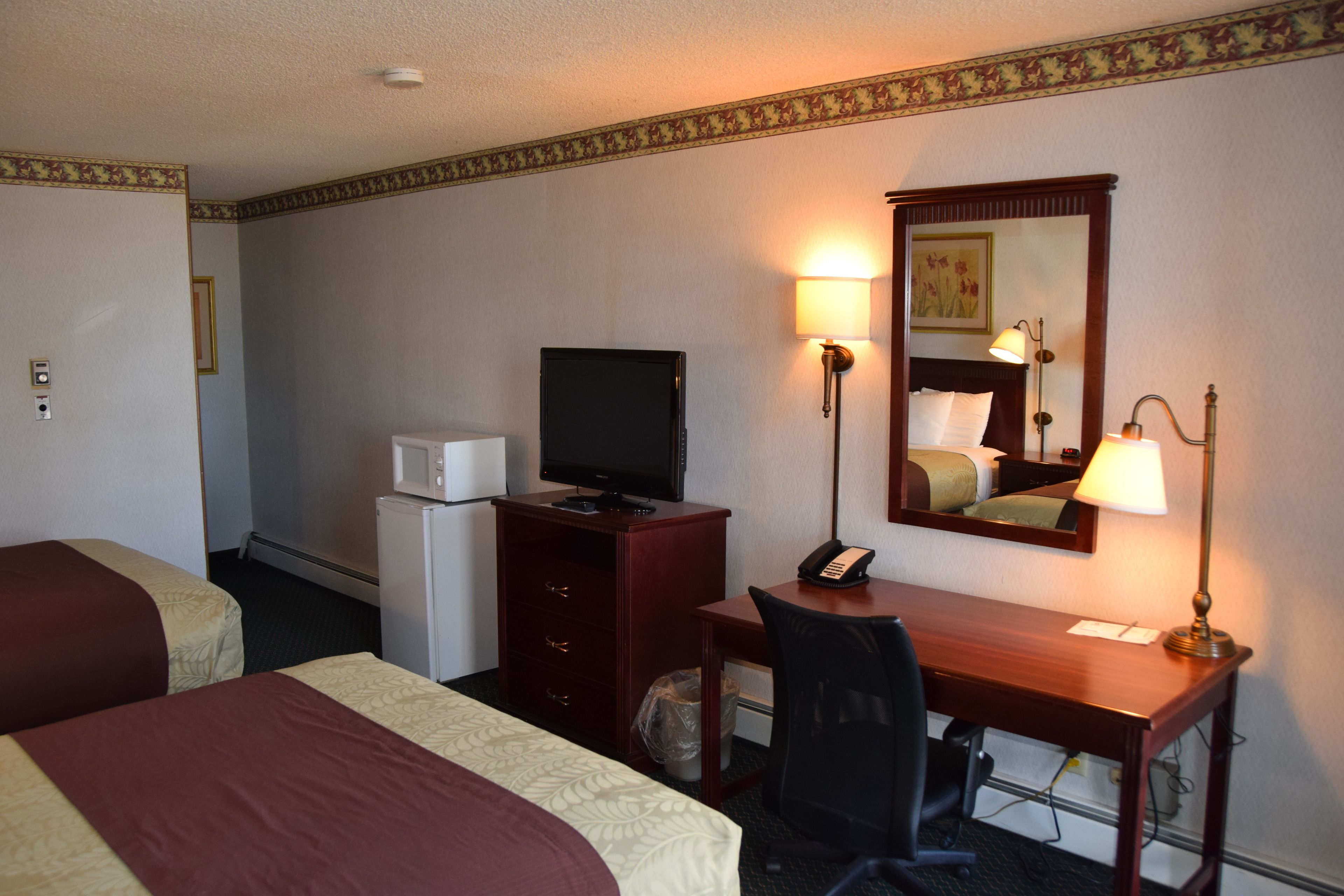 A hotel room with two beds, a desk with a computer, a telephone, a television, and a lamp.