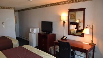 A hotel room with two beds, a desk with a computer, a telephone, a television, and a lamp.