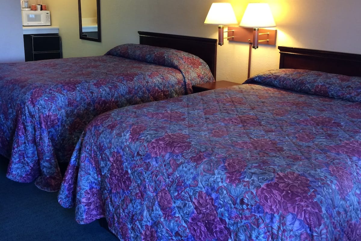 Ein Hotelzimmer mit zwei Betten, einem Nachttisch, einer Lampe, einer Mikrowelle und einem kleinen Schrank.