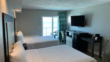 A hotel room with two beds, a desk, a television, and a view of the sea.