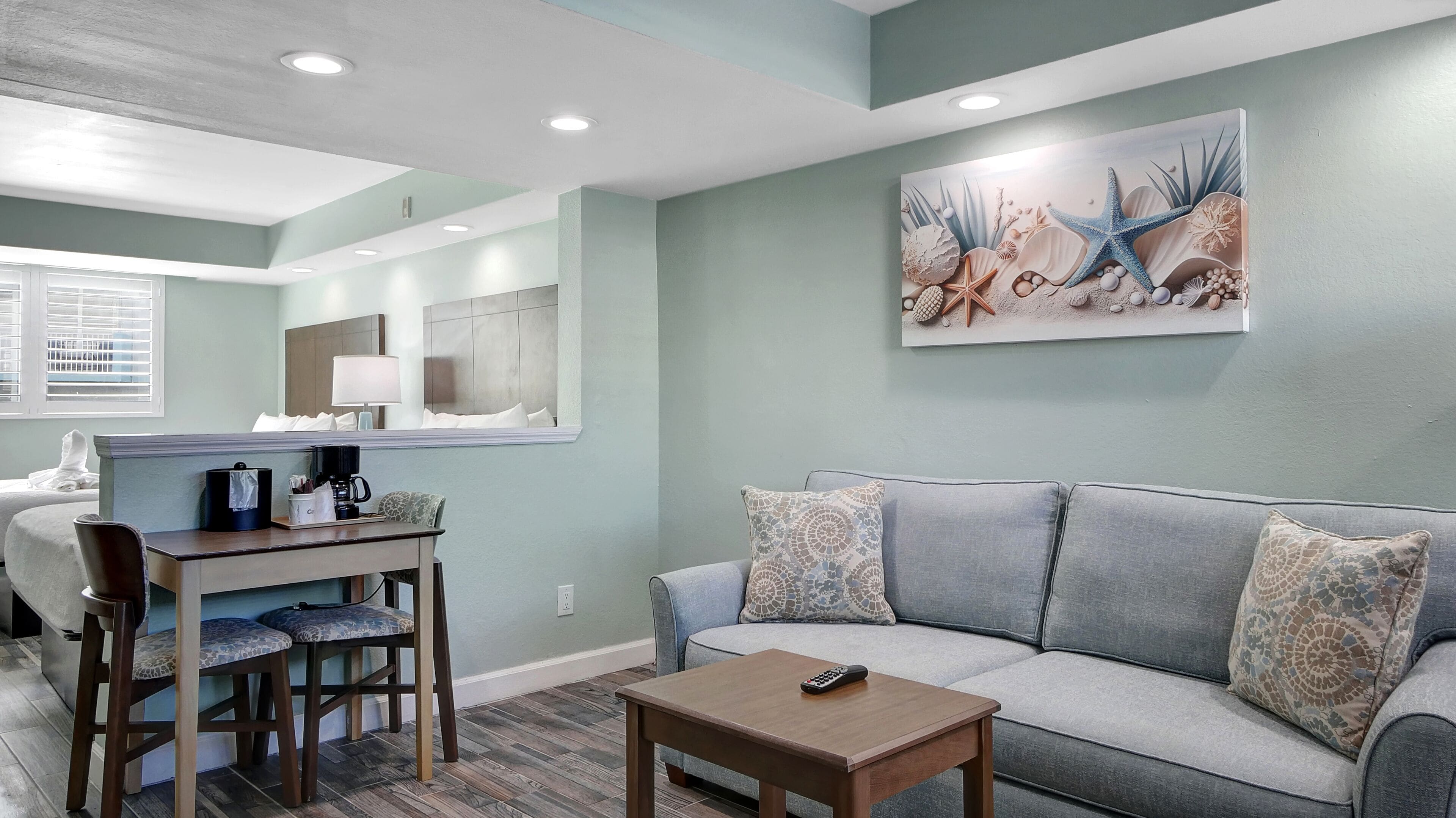 A modern living room with a grey sofa, a wooden coffee table, and a dining area with a table and chairs.
