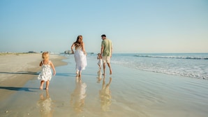 A family walking on a sandy beach with calm water and a clear sky. - Boardwalk Inn and Suites (Daytona Beach)