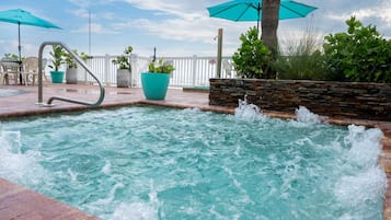Zona de piscina con fuente de agua, plantas en macetas y sombrillas.