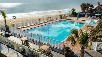 A pool area with a view of the beach, lounge chairs, and umbrellas.