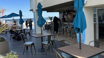 Un espace extérieur aménagé pour les repas, avec des tables et des chaises, des parasols bleus et une vue sur la mer.