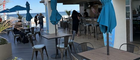 Un espace extérieur aménagé pour les repas, avec des tables et des chaises, des parasols bleus et une vue sur la mer.