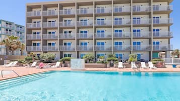 A multi-story hotel with a swimming pool, balconies, and lounge chairs.