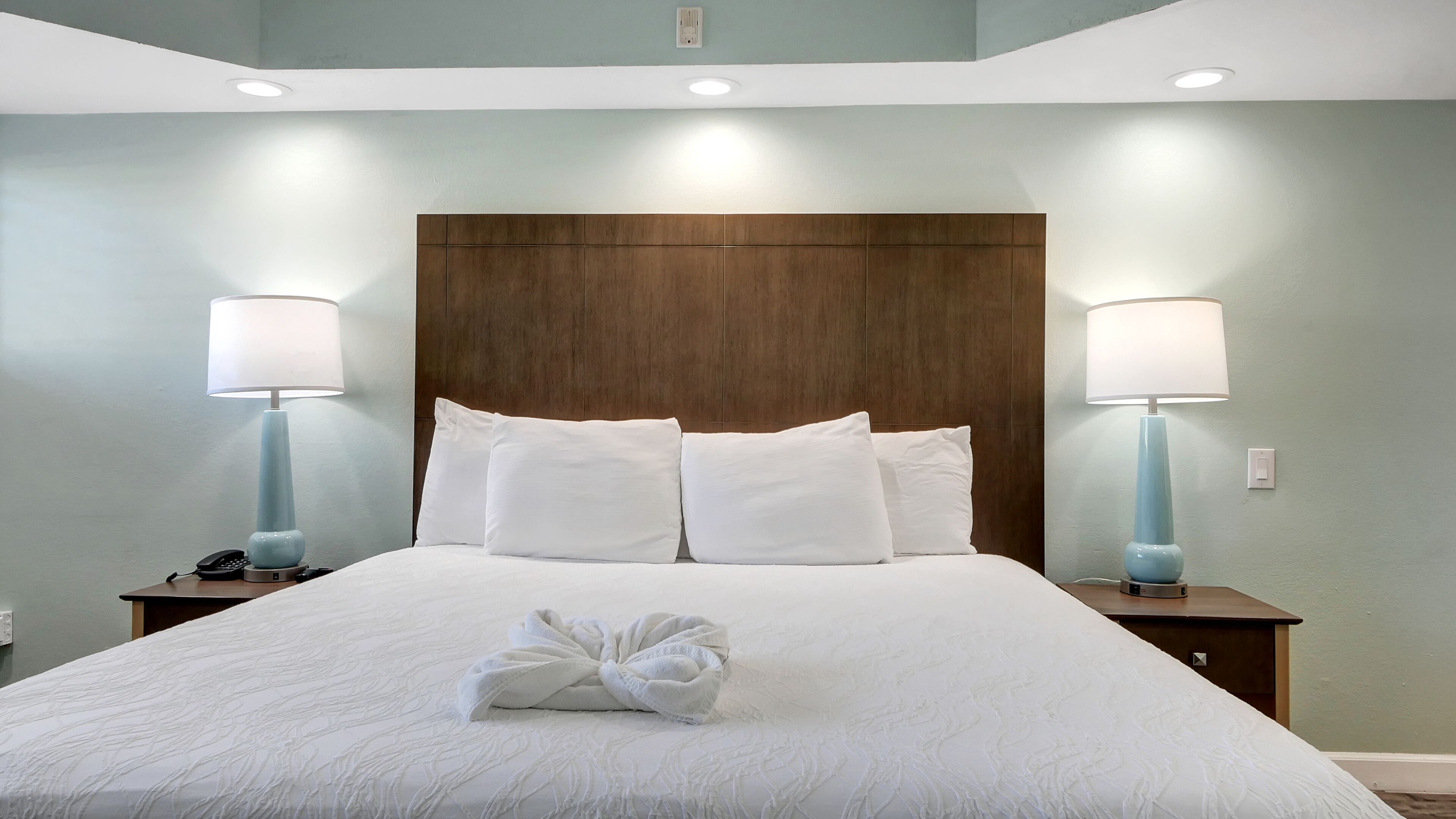 Una cama bien hecha con sábanas y almohadas blancas, dos lámparas de noche y un cabecero de madera.