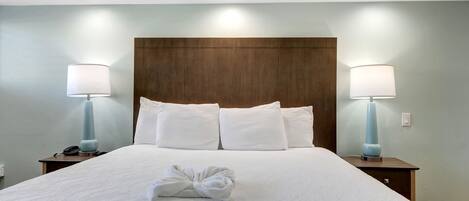 Una cama bien hecha con sábanas y almohadas blancas, dos lámparas de noche y un cabecero de madera.